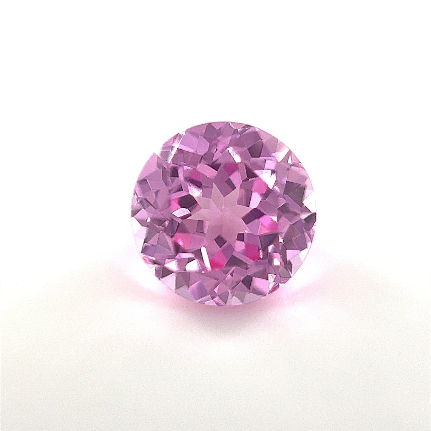 A 9mm Exceptional Round Lab Created Medium Pink Sapphire with faceted cuts is displayed on a plain white background, highlighting its sparkling medium pink tones and reflective surfaces.