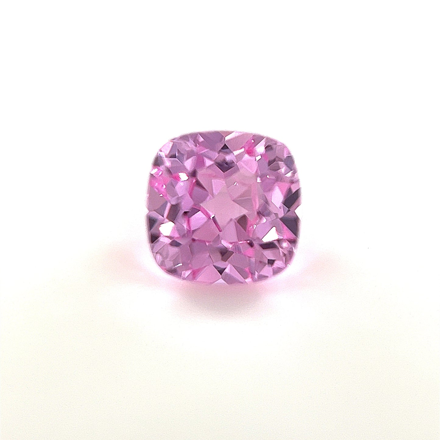 A 6mm Exceptional Cushion Lab Created Medium Pink Sapphire is shown against a white background, highlighting its vibrant color and sparkling clarity.