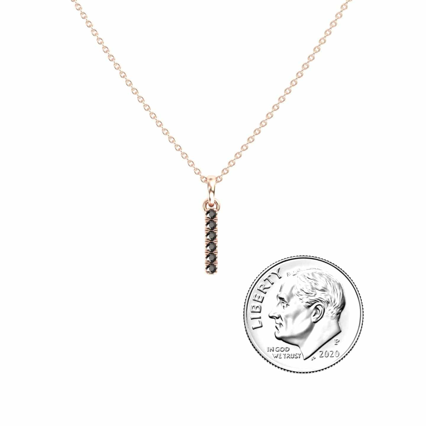 The Black Diamond Vertical Bar Necklace - Lalita features a delicate gold chain and a pendant with small black stones, shown next to a U.S. dime for size reference.