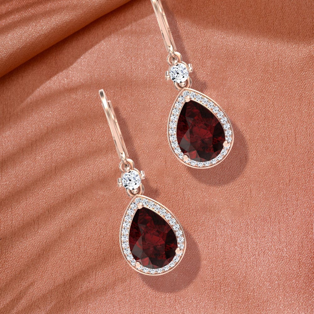 Pair of earrings with red garnet gemstones and rose gold accents on a brown fabric background