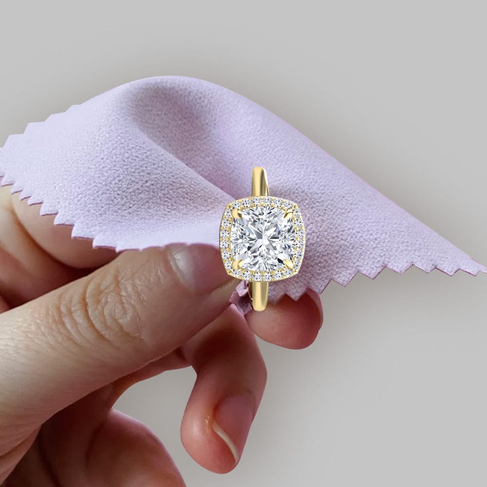Gold ring with a large diamond held by a hand on a light pink cloth.