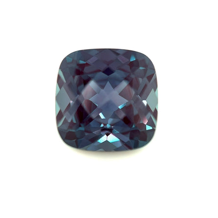 The 9mm Exceptional Cushion Checker Lab Created Alexandrite, featuring a cushion cut and deep blue hue, is shown against a white background.