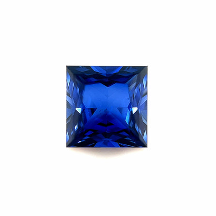The 8mm Exceptional Square Princess Created Blue Sapphire features angled facets that reflect light, displaying a vibrant, deep blue hue against a white background.