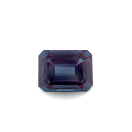 An emerald-cut, faceted 9.0x7.0 Exceptional Emerald Lab Created Alexandrite in blue-violet is displayed on a plain white background.
