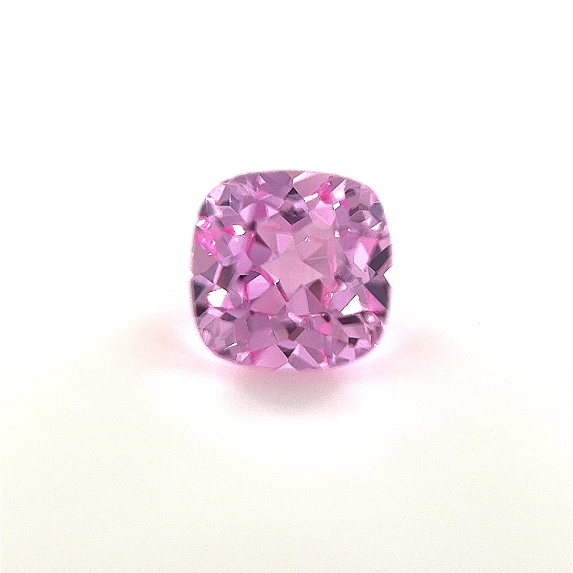 A 6mm Exceptional Cushion Lab Created Medium Pink Sapphire is shown against a white background, highlighting its vibrant color and sparkling clarity.
