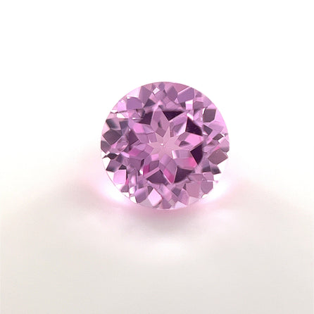 A 7mm Exceptional Round Lab Created Medium Pink Sapphire with brilliant faceting and vibrant medium pink hue is displayed on a clean white background, dazzling with clarity and elegance.