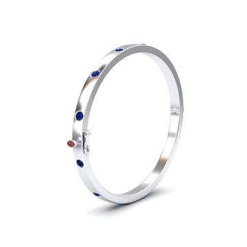 The Blue Sapphire Bezel-Set Bracelet - Flavia is a sleek silver bangle with evenly spaced round blue sapphires and a small red circular accent marked 15, shown against a plain white background.
