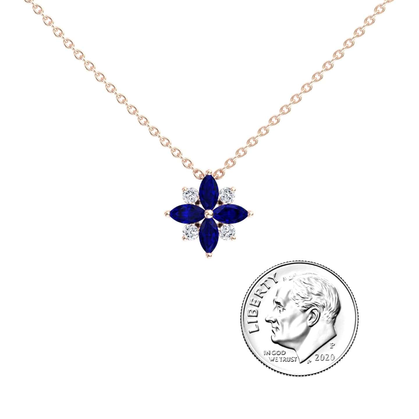 The Blue Sapphire & Diamond Flower Necklace - Keira features a flower-shaped pendant with blue sapphires and diamonds, shown beside a 2020 U.S. dime for size comparison.