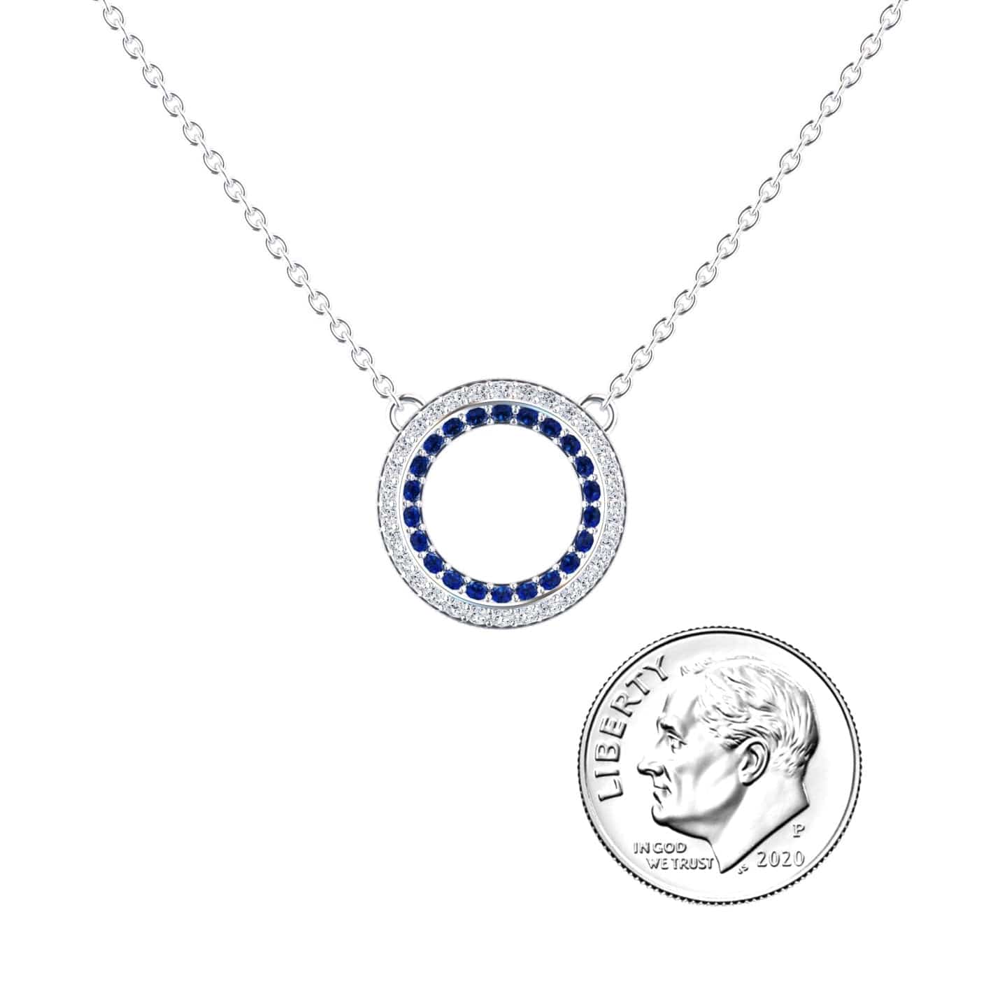 The Blue Sapphire & Diamond Double Halo Circle Necklace - Mona features a circular pendant with blue and clear stones, shown beside a U.S. dime for size reference.