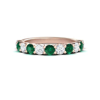 A rose gold half eternity wedding ring with alternating emerald and diamond gemstones.