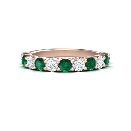 A rose gold half eternity wedding ring with alternating emerald and diamond gemstones.