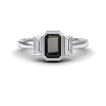 The Black & White Diamond Three-Stone Art Deco Ring - Ivy features a rectangular black gemstone center, flanked by two smaller baguette-cut clear stones on each side, shown against a white background.