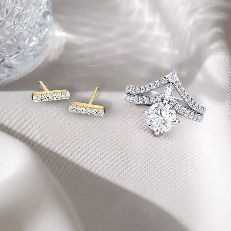 Pair of gold bar earrings and a silver ring with a diamond on a soft gray background