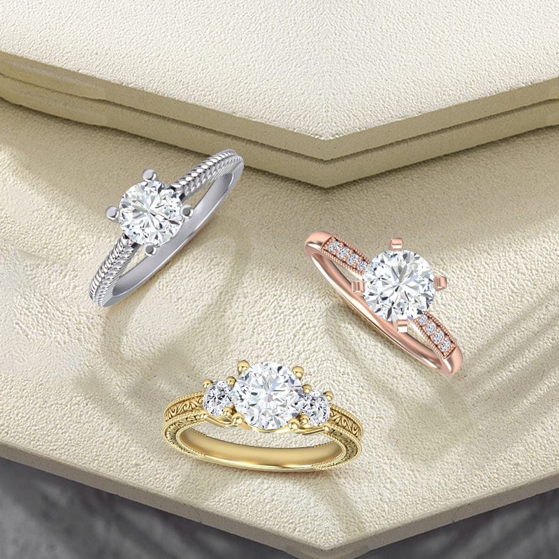 Three diamond rings in gold, silver, and rose gold on a textured beige surface.